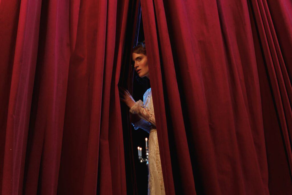 woman standing behind red curtain